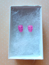 Load image into Gallery viewer, A pair of pink skull shaped earrings in a white paper jewelry box.