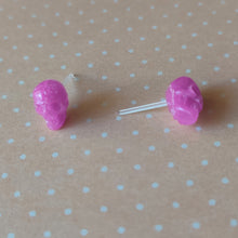 Load image into Gallery viewer, a pair of pink skull shaped earrings displayed on a pale orange and white polka dot background.