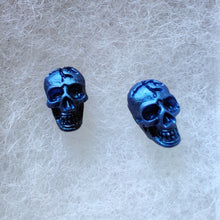 Load image into Gallery viewer, A close of picture of metallic  sapphire colored skull earrings attached to plastic posts.