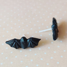 Load image into Gallery viewer, One pair of flat backed bat earrings with relief sculpted detail. Stud earrings are displayed on a pale orange and white polka dot background.