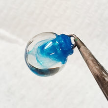 Load image into Gallery viewer, a clear miniature Christmas bauble held by the top with small thin pliers. Swirls of a shimmering blue are inside the clear.