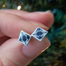 Load image into Gallery viewer, Small, diamond shaped stud earrings  with an abstract white and silver design held between finger and thumb.