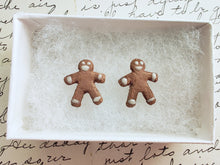 Load image into Gallery viewer, A pair of earrings made to look like gingerbread men. The earrings are inside a white paper jewelry box.