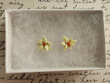 Load image into Gallery viewer, A pair of white poinsettia earrings with red centers and green veins inside a white paper jewelry box.