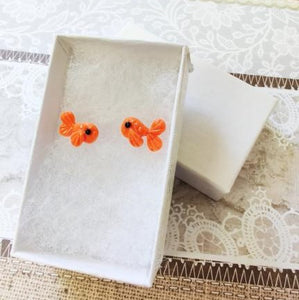 Two orange fish stud earrings in a white paper jewelry box