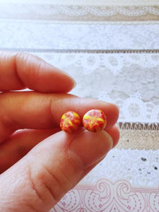 A pair of red and yellow stud earrings held between finger and thumb