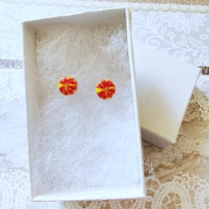 A pair of round yellow and red stud earrings inside a white paper jewelry box