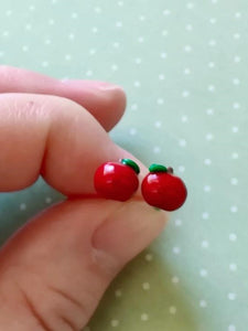 A pair of miniature apple stud earrings held between finger and thumb