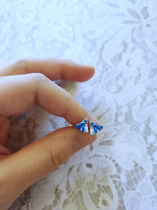 A pair of blue, white, and silver triangle earrings held between finger and thumb