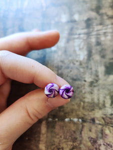 Purple, gold and white swirl earrings held between finger and thumb