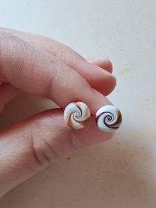 Purple, gold and white swirl earrings held between finger and thumb
