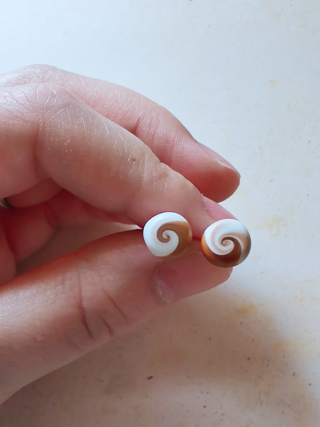 Gold and white swirl earrings held between finger and thumb