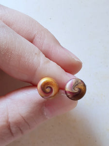 Gold and purple swirl earrings held between finger and thumb