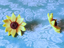 Load image into Gallery viewer, Two sunflower earrings placed on a flat surface one facing forward and one facing sideways.
