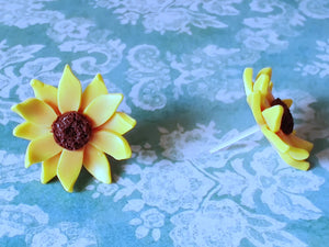 Two sunflower earrings placed on a flat surface one facing forward and one facing sideways.