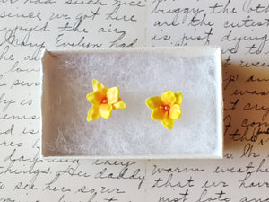 A pair of yellow and orange daylily earrings in a white paper jewelry box.