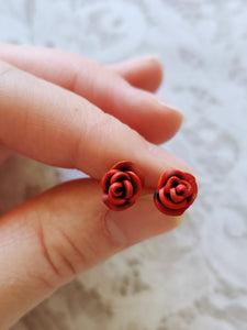 A pair of red and black rose flower earrings held between finger and thumb.