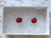 Load image into Gallery viewer, A pair of red and black rose flower earrings inside a white paper jewelry box.
