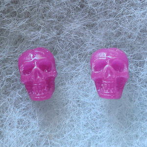 Pink skull shaped stud earrings that shimmer purple in the light. 