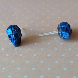 A close of picture of metallic  sapphire colored skull earrings displayed on a pale orange background with white polka dots.