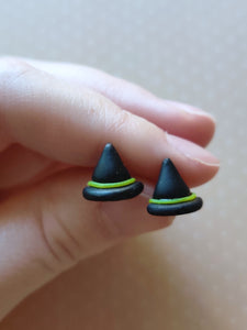 A pair of black witches hats with yellow bands made into flat backed stud earrings. Earrings are displayed between finger and thumb.