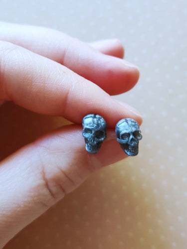 Grey colored skull stud earrings that shimmer silvery in the light. 