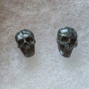A close of of grey colored skull stud earrings that shimmer silvery in the light. 