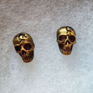 A close of picture of faux aged gold skull earrings attached to plastic posts. 