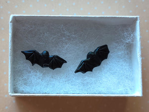One pair of flat backed bat earrings with relief sculpted detail. Stud earrings are displayed in a white paper jewelry box. 