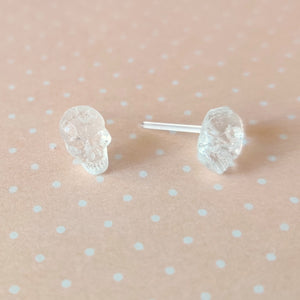 One pair of clear skull stud earrings displayed on a pale orange and white polka dot background.