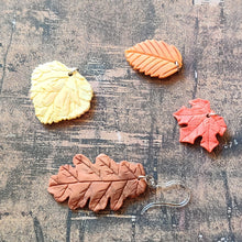 Load image into Gallery viewer, A picture showing a group of fall colored leaves for an example of various colors that the leaves could be customized to look. The group shows a red maple leaf, a rust orange beach leaf, a yellow aspen leaf, and a rust brown oak leaf.
