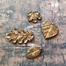 Load image into Gallery viewer, A group of polymer clay leaves showing a gold finish similar to plaited or brushed gold. The leaves are shaped like one leaf each of a red maple, oak, beach, and aspen leaf.
