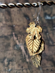 One dangle earring with fall leaves cascading down as if stacked on top of each other. A maple leaf is on top, followed by a beech, an aspen, and a oak.