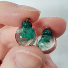 Load image into Gallery viewer, Two miniature Christmas ornament baubles in a clear color with silvery green swirls inside. The are held between finger and thumb. 
