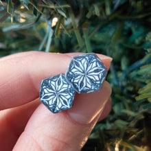 Load image into Gallery viewer, Two hexagon shaped earrings  with a kaleidoscope pattern reminiscent of a snowflake or stained glass. the earrings are held between finger and thumb in front of an artificial Christmas tree branch. 
