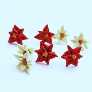 Two pairs each of white and red Poinsettia earrings displayed on white paper. One pair of each color is in focus in the foreground, and one of each color is out of focus in the background. 