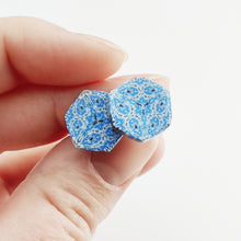 Load image into Gallery viewer, Two hexagon shaped earrings with intricate white, silver and blue patterns held between finger and thumb.
