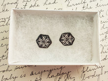 Load image into Gallery viewer, Two hexagon shaped earrings  with a kaleidoscope pattern reminiscent of a snowflake or stained glass. The earrings are inside a white paper jewelry box. 
