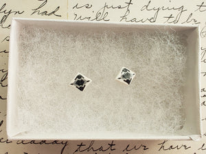 Small, diamond shaped stud earrings  with an abstract white and silver design inside a white paper jewelry box.