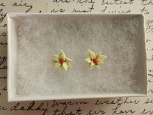 Load image into Gallery viewer, A pair of white poinsettia earrings with red centers and green veins inside a white paper jewelry box. 
