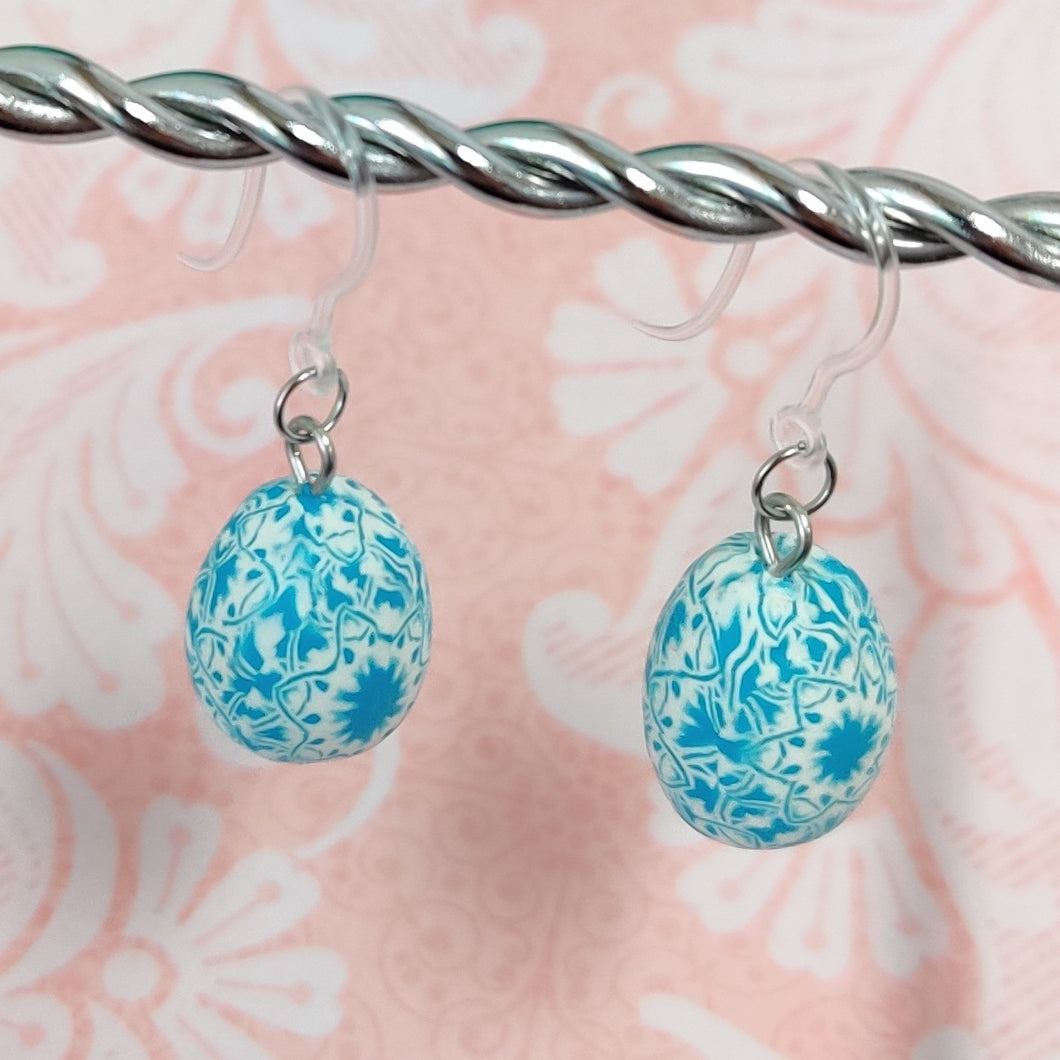 Patterned Easter egg shaped dangle earrings in a blue and white color hanging from a silver wire. 
