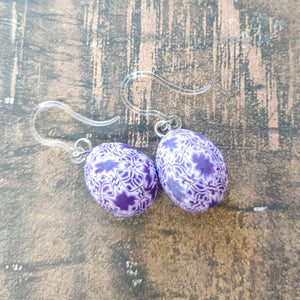 Patterned Easter egg shaped dangle earrings in a purple and white one a brown paper background.